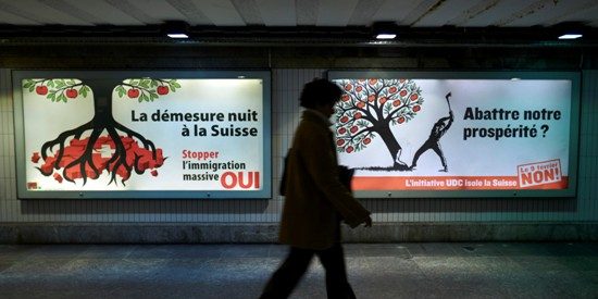 A woman walks past two immigration campaign posters in Lausanne February 4, 2014. With foreigners making up 23 percent of Switzerland's population of 8 million, the Swiss will vote on February 9 on a proposal to re-impose quotas on migrants from the European Union. The right-wing Swiss People's Party (SVP) wants Switzerland to seize back control over immigration by reintroducing quotas, renegotiating free movement of people with the EU, introduced in 2002 and asking employers to give national preference when filling jobs. REUTERS/Denis Balibouse (SWITZERLAND - Tags: SOCIETY IMMIGRATION BUSINESS EMPLOYMENT POLITICS) - RTX187EE